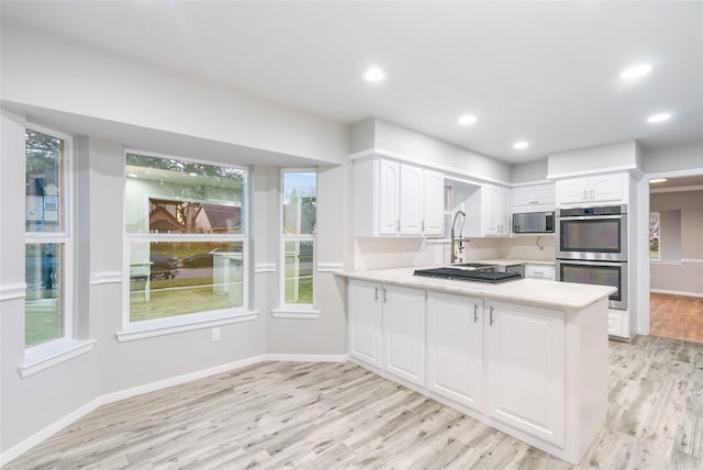 kitchen featuring kitchen peninsula, stainless steel appliances, light wood-type flooring, white cabinets, and sink