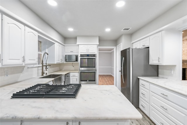 kitchen with tasteful backsplash, sink, light stone countertops, stainless steel appliances, and white cabinets