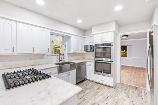 kitchen with backsplash, sink, white cabinetry, light hardwood / wood-style flooring, and stainless steel appliances