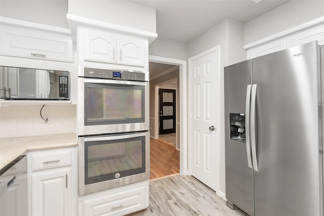 kitchen with tasteful backsplash, white cabinets, stainless steel appliances, and light wood-type flooring