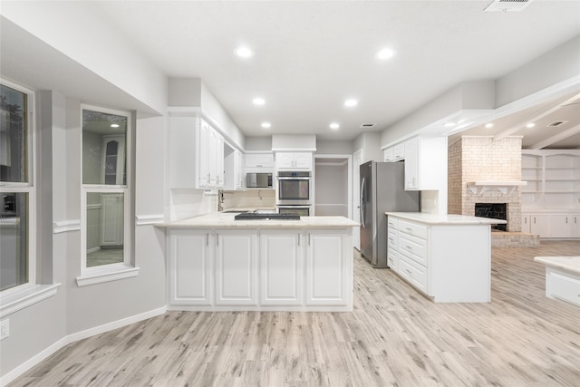 kitchen with white cabinets, stainless steel appliances, a fireplace, light hardwood / wood-style floors, and kitchen peninsula