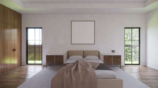 bedroom with light hardwood / wood-style floors and a raised ceiling