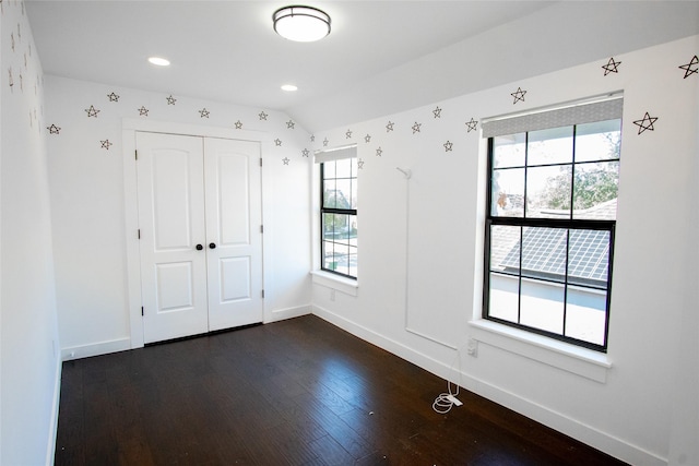 empty room featuring lofted ceiling, a healthy amount of sunlight, and dark hardwood / wood-style flooring