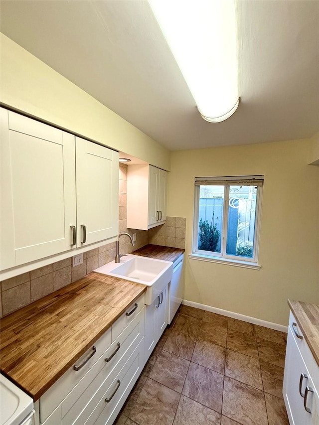 kitchen featuring butcher block countertops, dishwasher, white cabinetry, sink, and backsplash