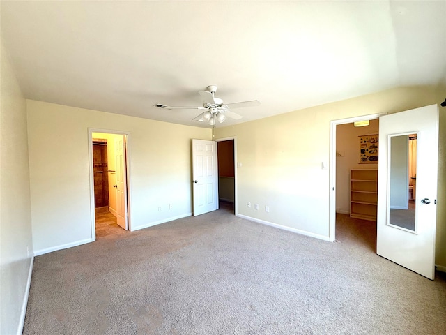 unfurnished bedroom featuring ceiling fan, a walk in closet, a closet, and light carpet