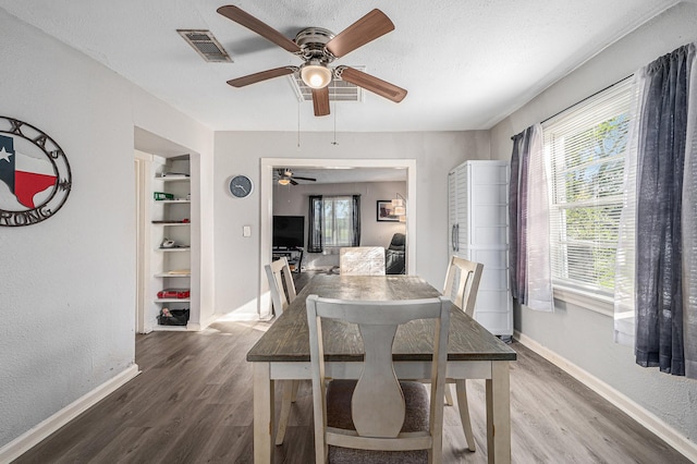 dining room with built in shelves, wood-type flooring, and a textured ceiling