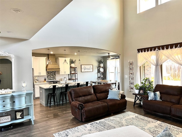 living room with ceiling fan, dark hardwood / wood-style flooring, and a towering ceiling