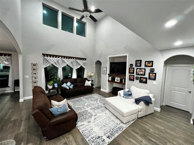 living room with ceiling fan, dark wood-type flooring, and a towering ceiling