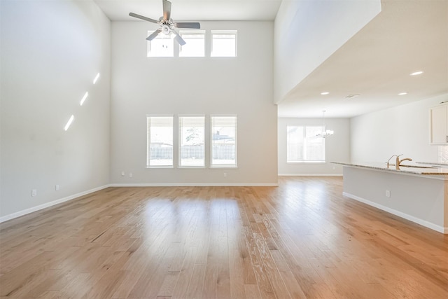 unfurnished living room featuring sink, ceiling fan with notable chandelier, light hardwood / wood-style flooring, and a towering ceiling