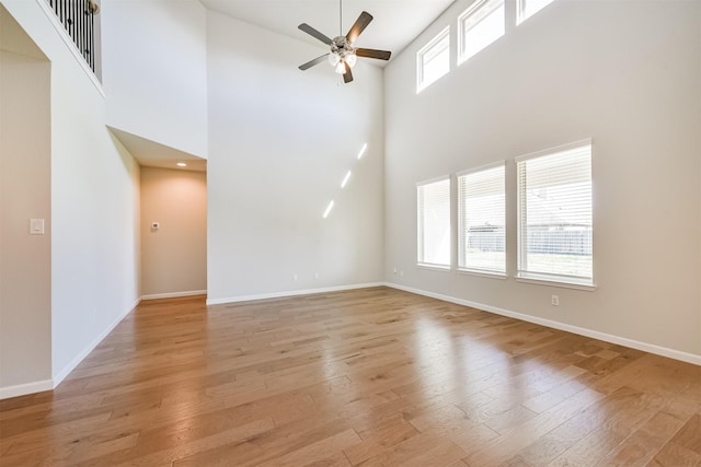 unfurnished living room with light hardwood / wood-style floors, ceiling fan, and a high ceiling