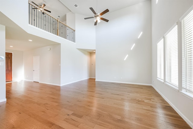 unfurnished living room featuring ceiling fan, light hardwood / wood-style floors, and a high ceiling