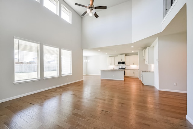 unfurnished living room featuring ceiling fan with notable chandelier and light wood-type flooring