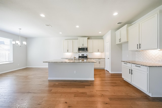 kitchen with light stone countertops, appliances with stainless steel finishes, a center island with sink, and white cabinets