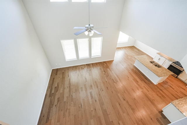 unfurnished living room featuring a towering ceiling, light hardwood / wood-style floors, and ceiling fan