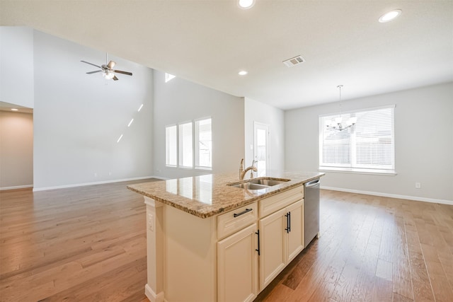 kitchen with dishwasher, sink, hanging light fixtures, light stone counters, and a center island with sink