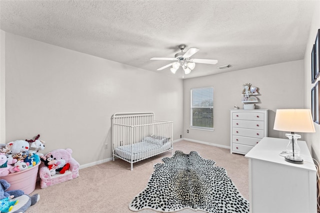 bedroom with ceiling fan, light colored carpet, a textured ceiling, and a crib