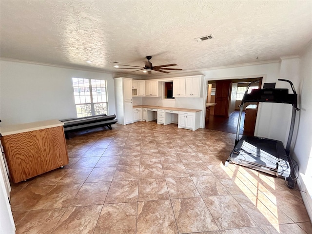 kitchen featuring a textured ceiling, built in desk, white cabinetry, ornamental molding, and ceiling fan