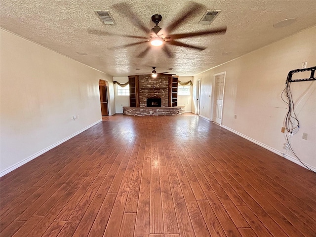 unfurnished living room with ceiling fan, dark wood-type flooring, a textured ceiling, and a brick fireplace