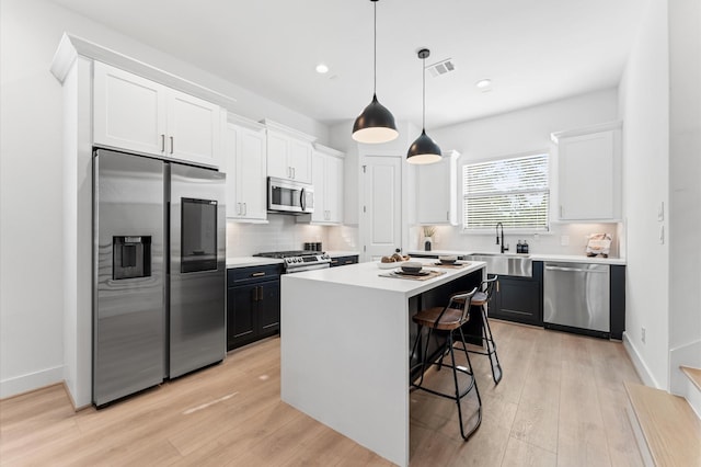 kitchen with stainless steel appliances, white cabinetry, a center island, and decorative light fixtures