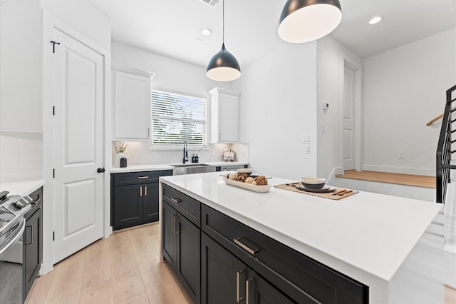 kitchen featuring a kitchen island, decorative light fixtures, sink, white cabinets, and electric stove