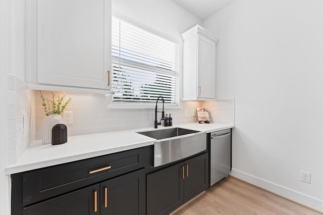 kitchen featuring sink, white cabinetry, stainless steel dishwasher, light hardwood / wood-style floors, and decorative backsplash