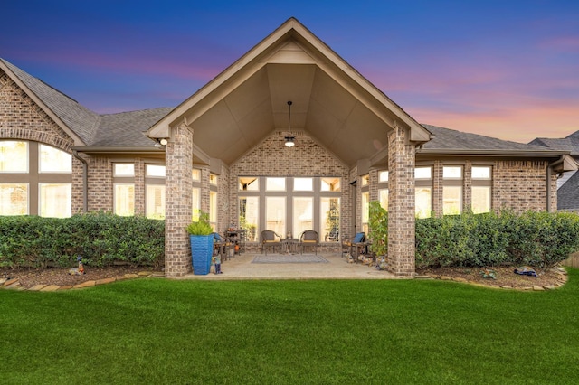 back house at dusk with a patio area and a lawn