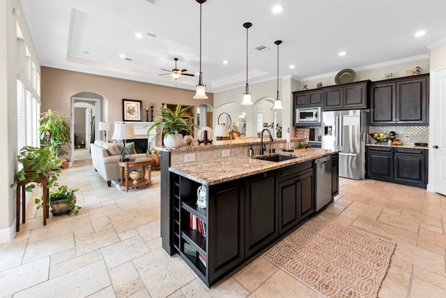 kitchen with an island with sink, ceiling fan, stainless steel appliances, pendant lighting, and sink