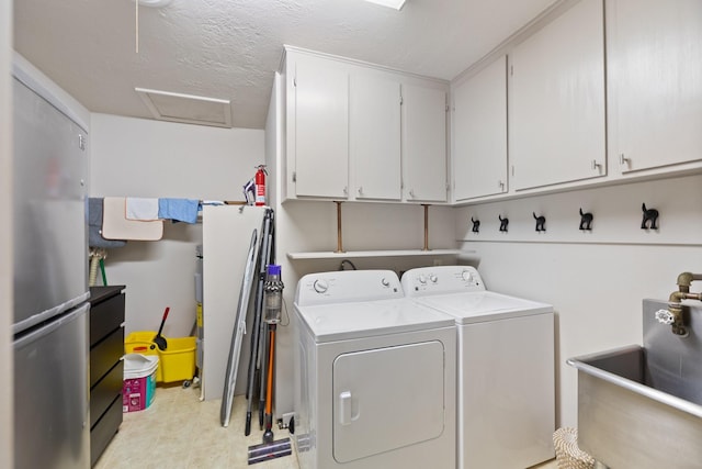 clothes washing area with washer and dryer, cabinets, a textured ceiling, and sink