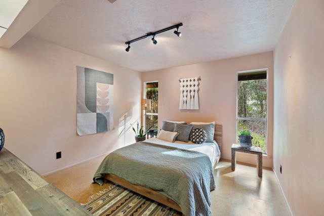 bedroom with a textured ceiling, rail lighting, and multiple windows