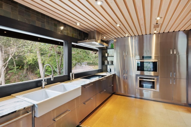 kitchen with exhaust hood, stainless steel appliances, light stone counters, and sink