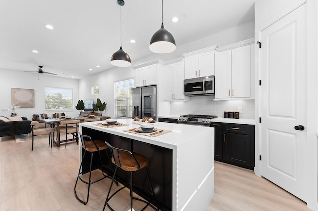 kitchen with a kitchen island, appliances with stainless steel finishes, a breakfast bar, white cabinetry, and hanging light fixtures