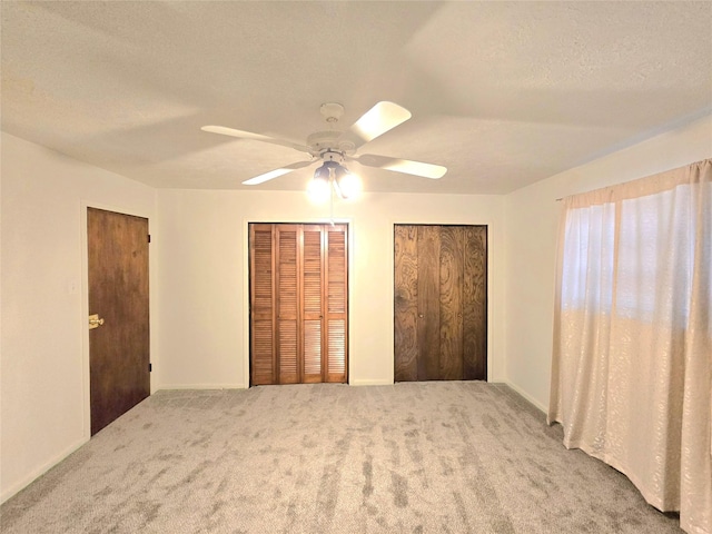 unfurnished bedroom featuring a textured ceiling, ceiling fan, carpet, and multiple closets