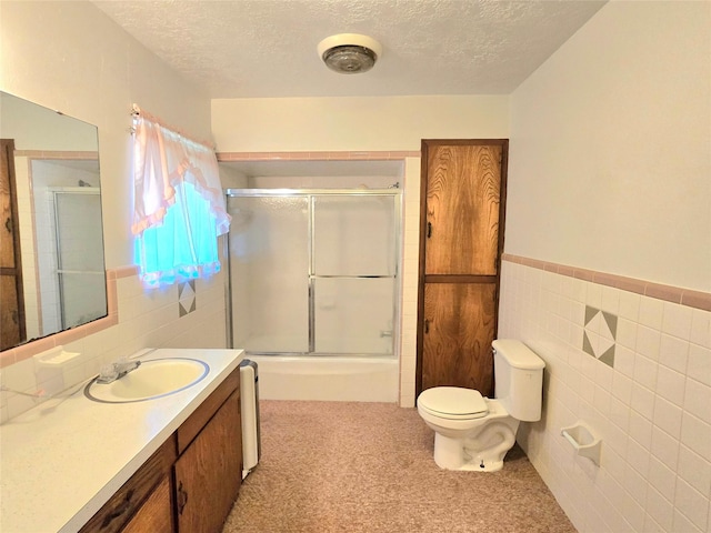 full bathroom with toilet, vanity, tile walls, a textured ceiling, and shower / bath combination with glass door