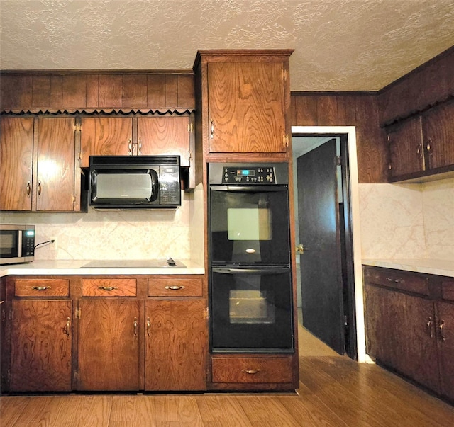 kitchen with black appliances, wood walls, and light hardwood / wood-style flooring