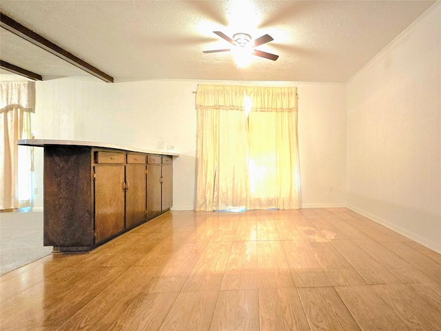 unfurnished room featuring ceiling fan, light wood-type flooring, beamed ceiling, and a textured ceiling