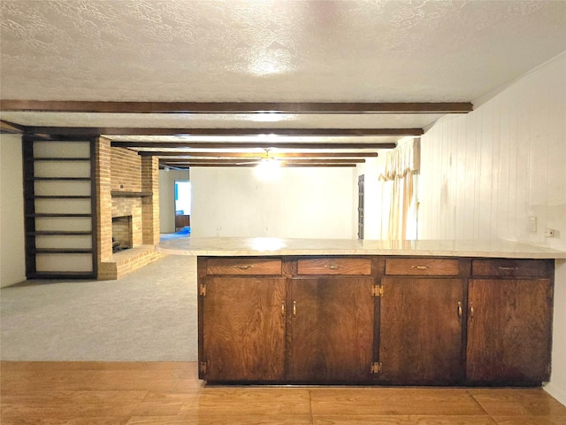 kitchen with a textured ceiling, light carpet, beam ceiling, and a fireplace