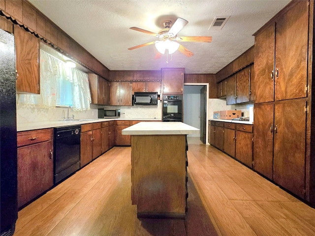 kitchen featuring a textured ceiling, black appliances, a center island, sink, and ceiling fan