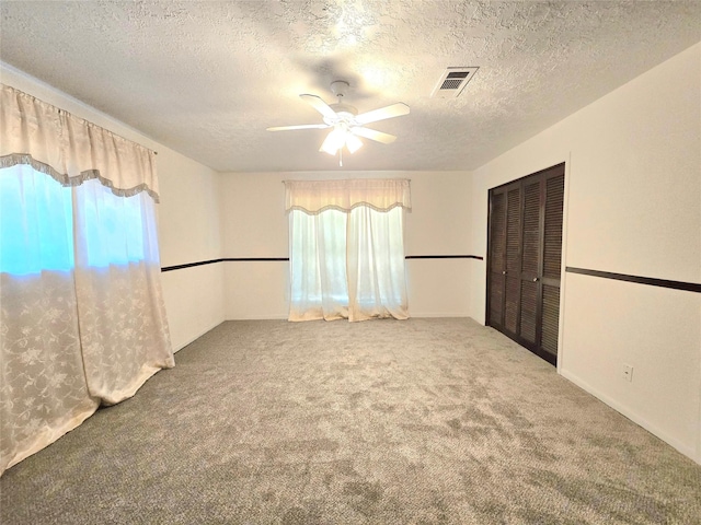 unfurnished room featuring carpet, ceiling fan, a wealth of natural light, and a textured ceiling