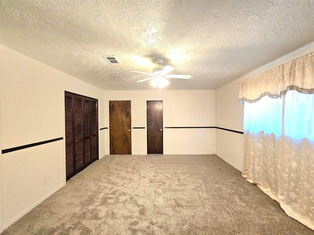 unfurnished bedroom featuring carpet floors, a textured ceiling, ceiling fan, and multiple closets