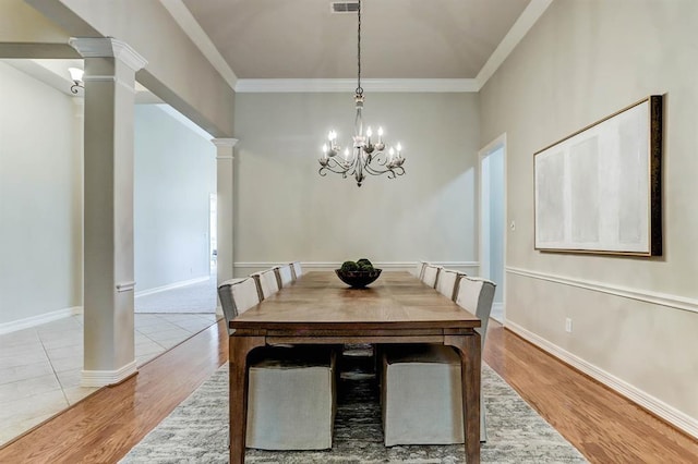 dining space featuring light wood-type flooring, a chandelier, crown molding, and decorative columns