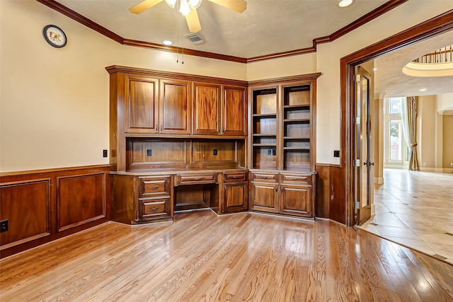 unfurnished office with ceiling fan, ornamental molding, built in desk, and light wood-type flooring