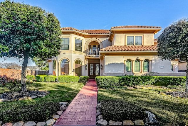 mediterranean / spanish-style home with a balcony, a front yard, and french doors