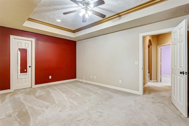 empty room with ceiling fan, light carpet, ornamental molding, and a raised ceiling