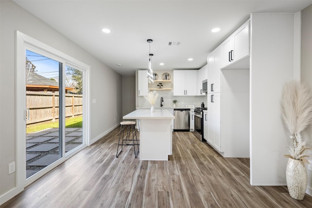 kitchen featuring stainless steel appliances, hanging light fixtures, a kitchen island, white cabinets, and a breakfast bar