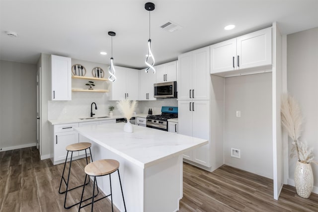 kitchen with appliances with stainless steel finishes, a center island, white cabinetry, sink, and light stone counters