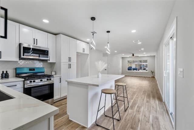 kitchen featuring white cabinets, stainless steel appliances, hanging light fixtures, ceiling fan, and light stone counters