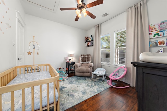 bedroom with ceiling fan, dark hardwood / wood-style floors, and a crib