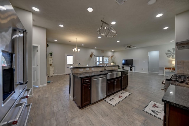 kitchen featuring dishwasher, hanging light fixtures, a kitchen island with sink, sink, and dark stone countertops