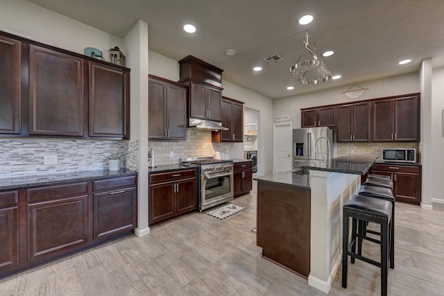 kitchen featuring a kitchen breakfast bar, appliances with stainless steel finishes, tasteful backsplash, dark stone countertops, and a center island with sink