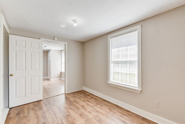 unfurnished bedroom featuring multiple windows, a textured ceiling, and light wood-type flooring